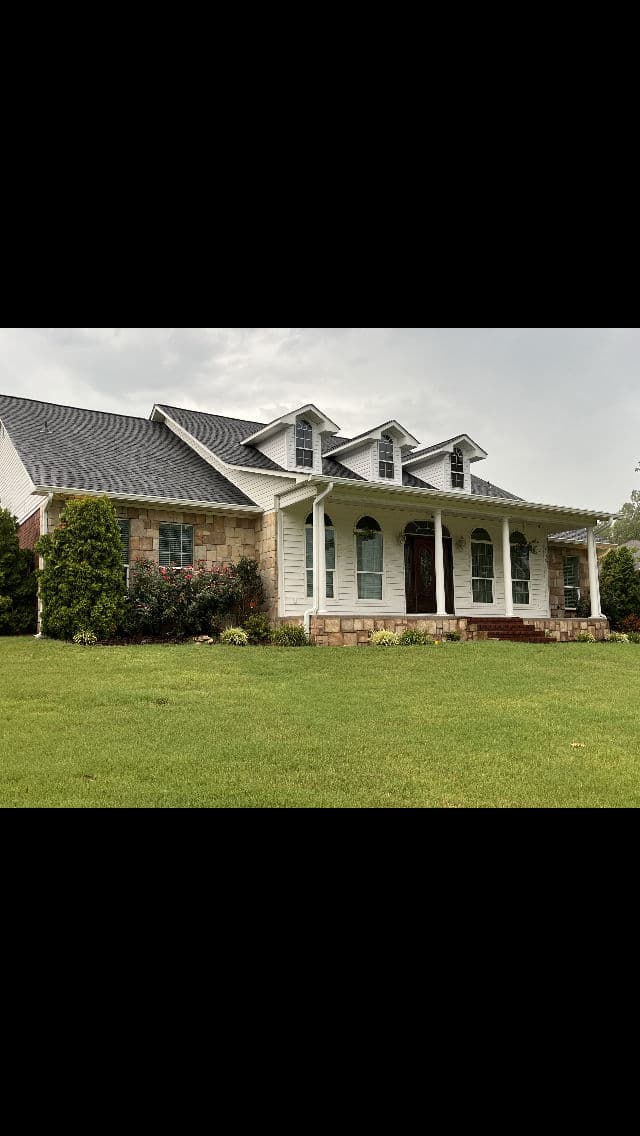 Modern two-story house with stone and siding exterior, lush green lawn, and landscaped garden.