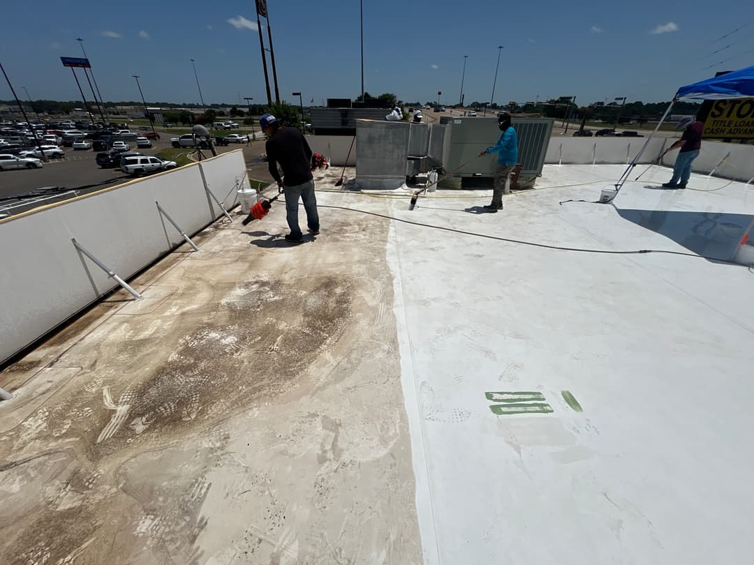 Workers applying sealant on a commercial building roof under a clear blue sky.