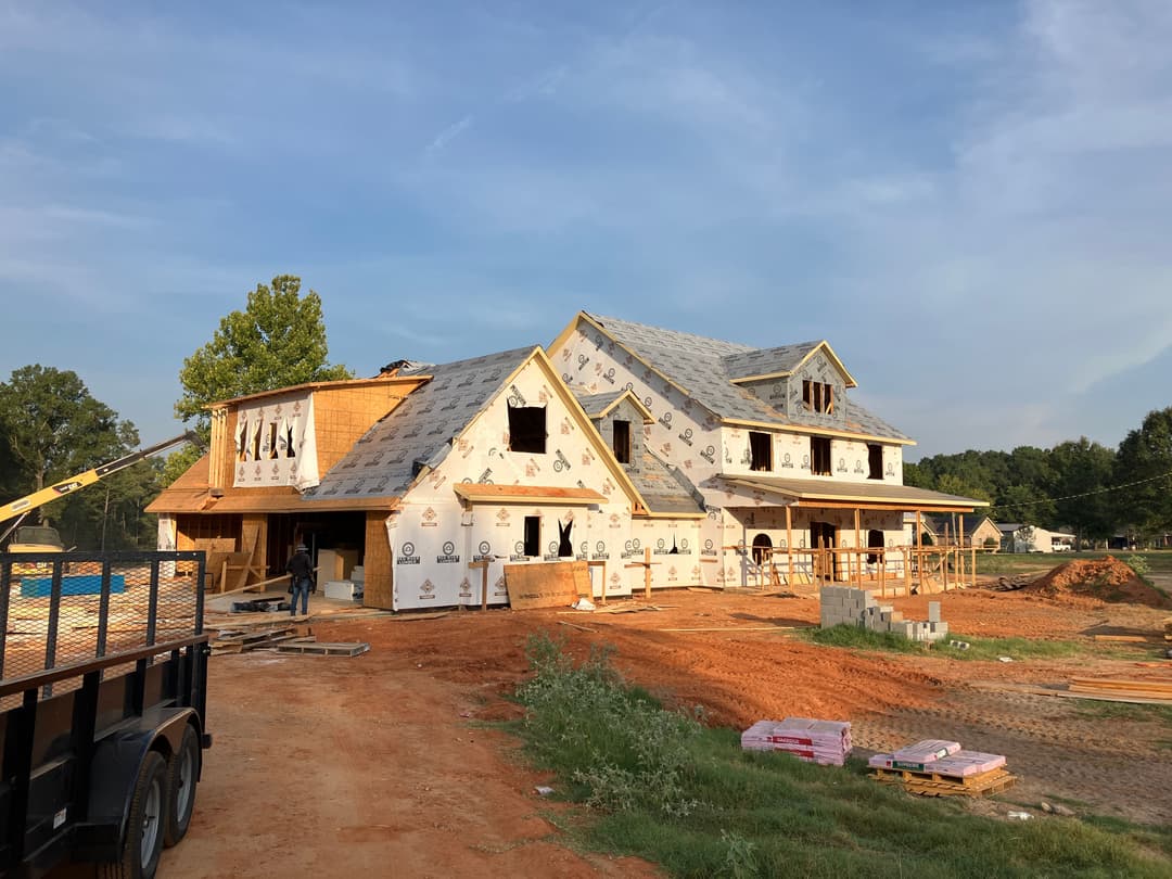 Newly constructed house under development with roofing and exterior wrap in progress.