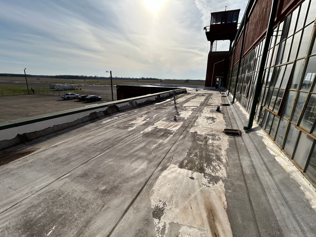 View of an industrial rooftop with weathered surface, overlooking an airfield and control tower.