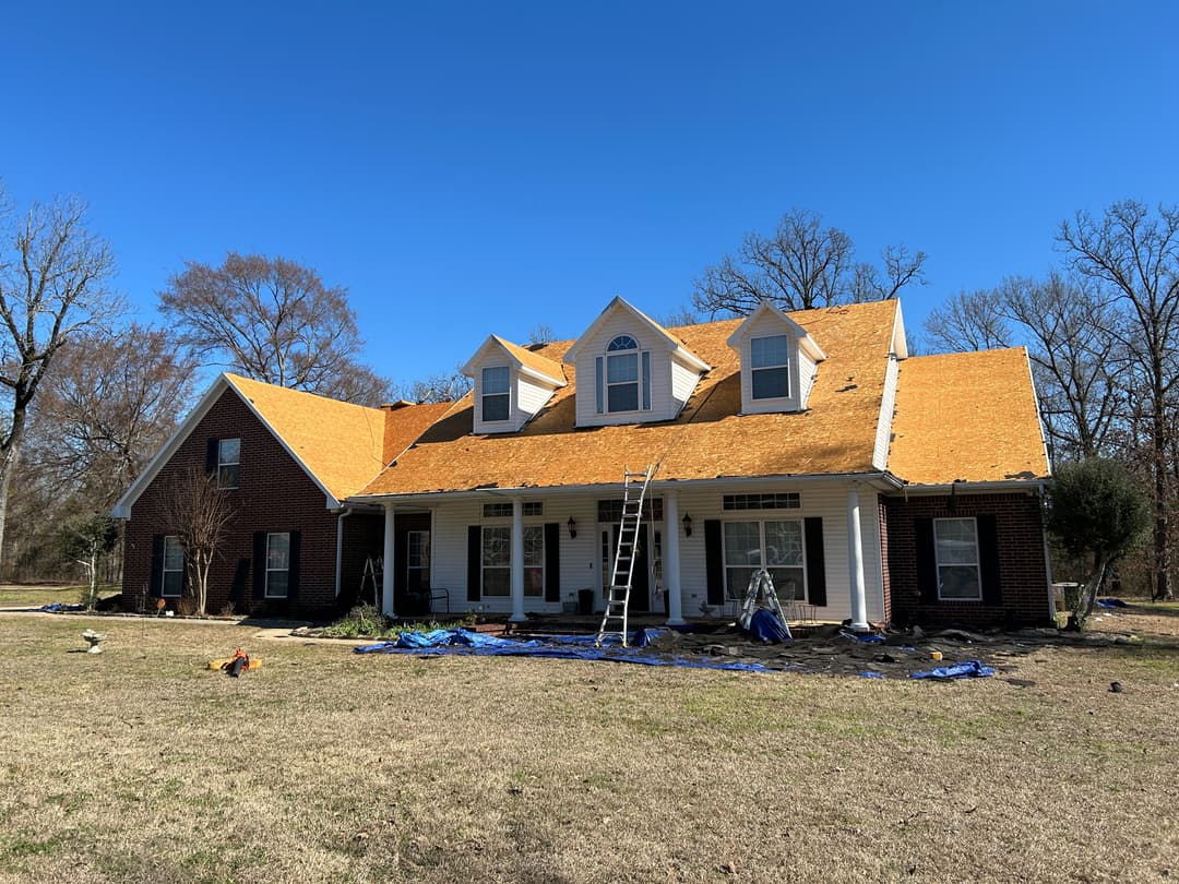 House with orange roof shingles under construction, blue sky, and renovation equipment visible.