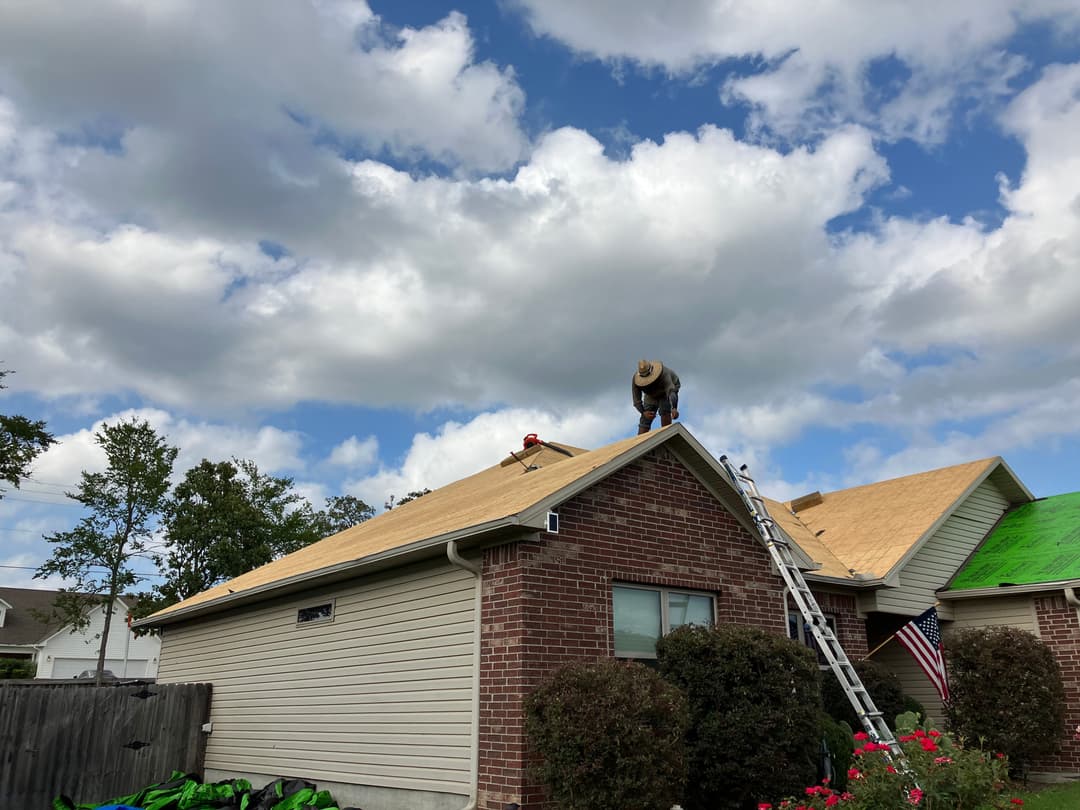 Roof repair in progress with workers on a house under a blue sky with clouds.