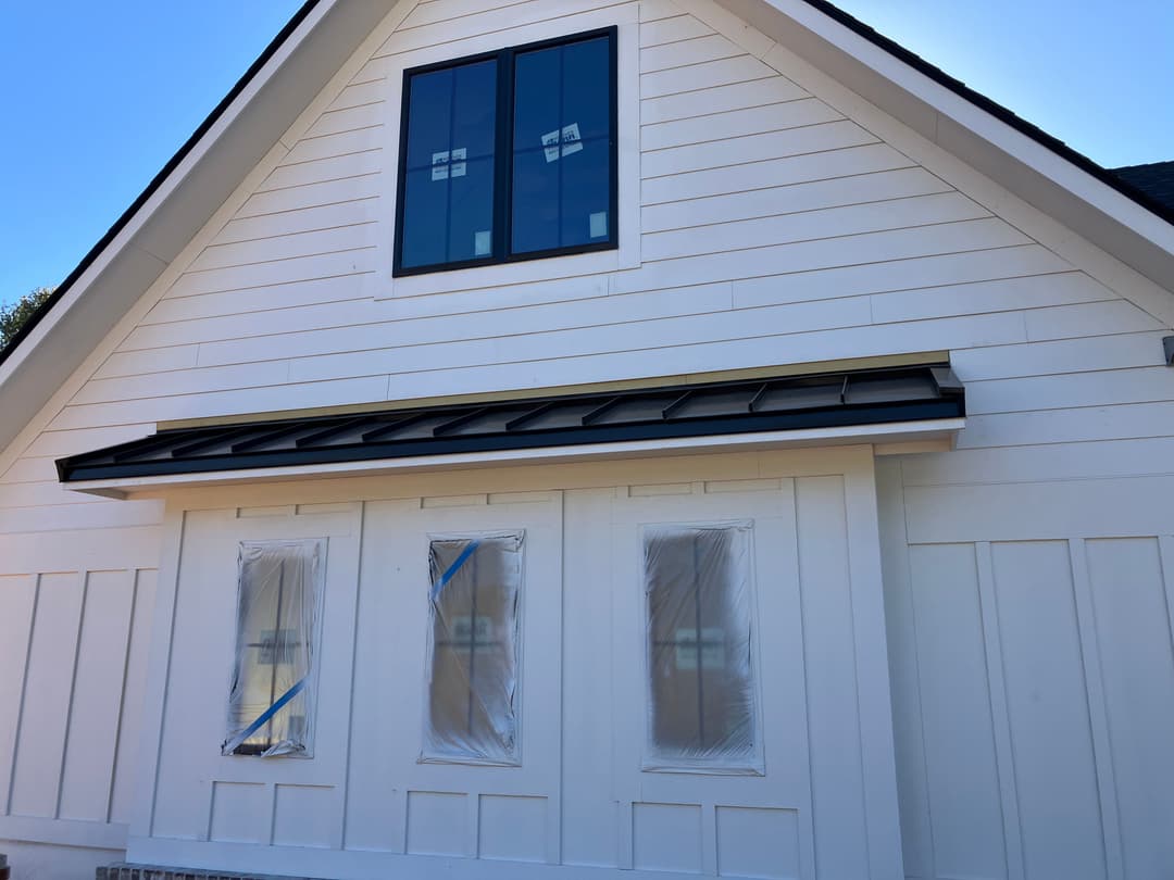 Modern white house exterior with large windows and protective coverings.
