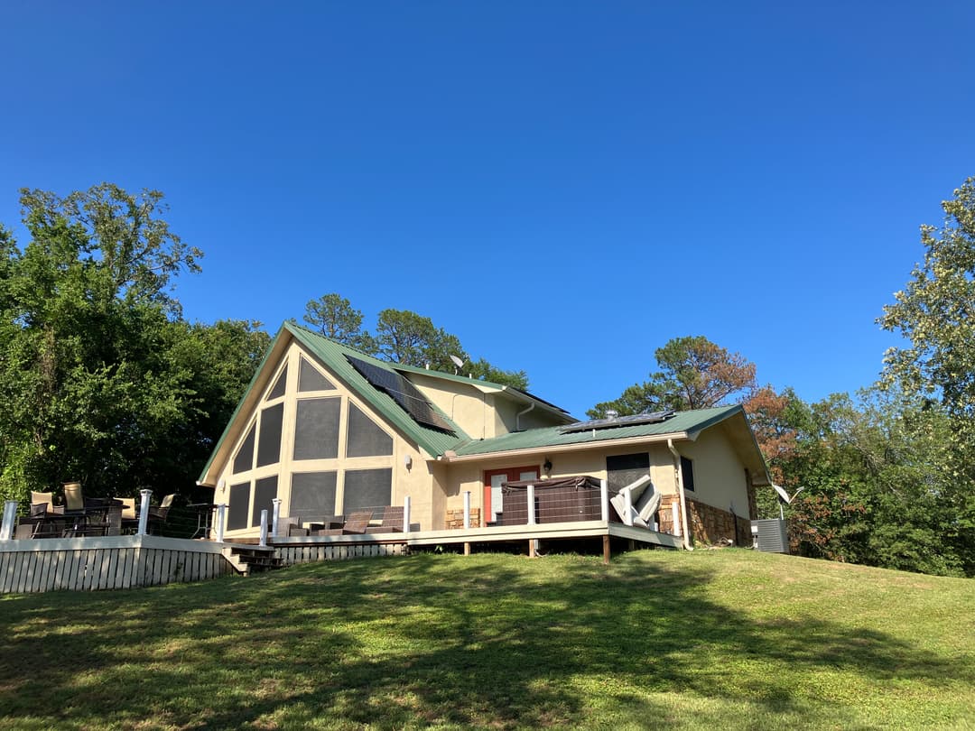 Modern house with solar panels on a green hill under a clear blue sky.