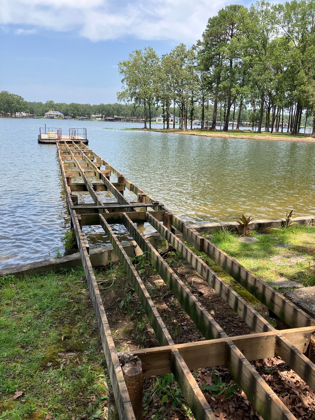Wooden dock frame leading to a calm lake surrounded by trees and greenery.