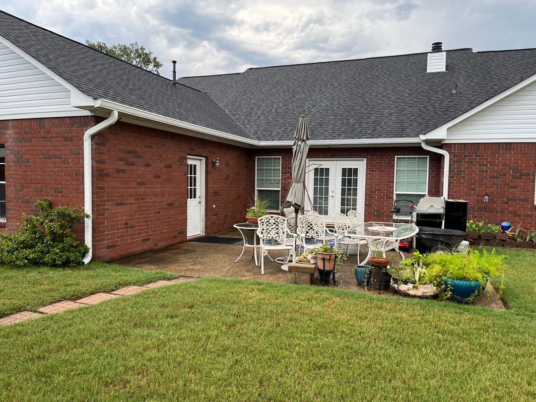 Brick house patio with white garden furniture, grill, and landscaping on a grassy yard.