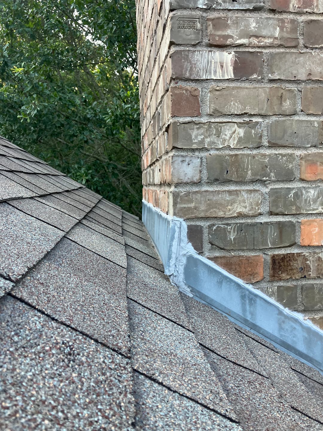Roof detail showing shingles and brick chimney with newly applied waterproofing sealant.