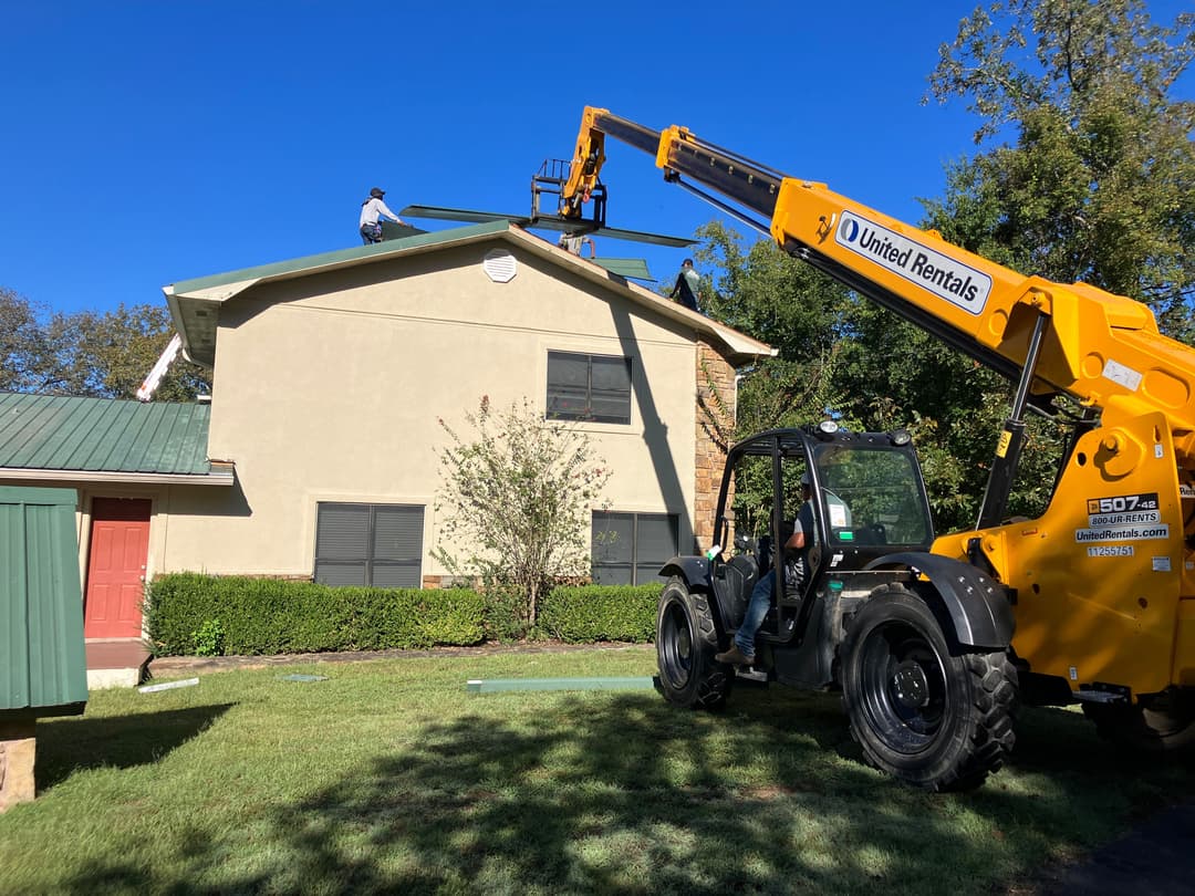 Workers installing a roof with a telehandler at a residential building on a sunny day.