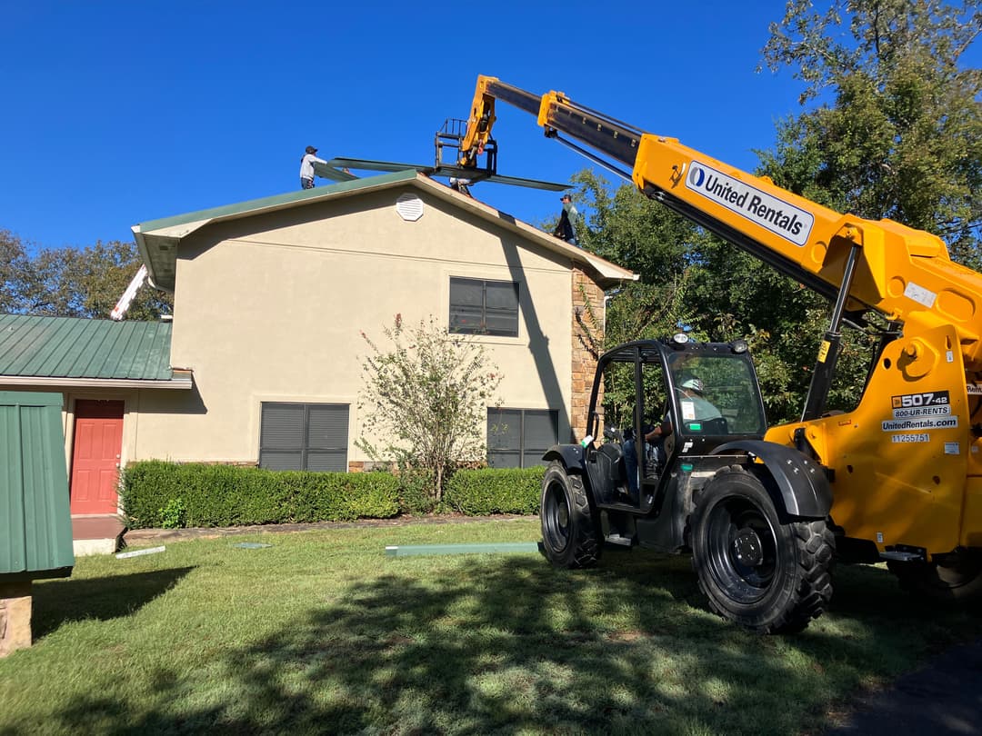 Construction worker on roof using telehandler for roofing project on a residential building.