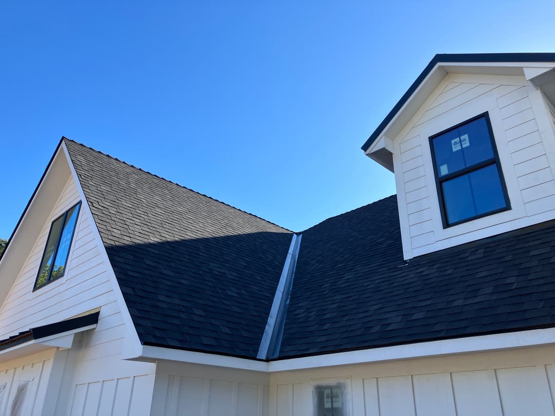 Modern house with a black shingle roof against a clear blue sky. Bright white siding.