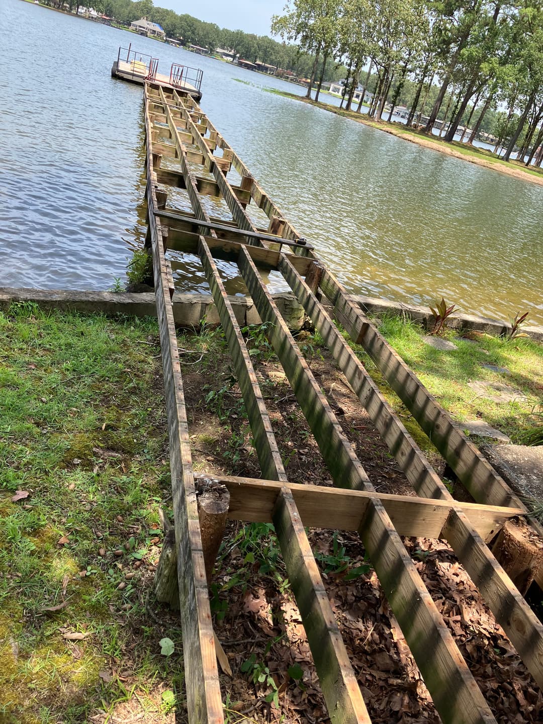 Wooden dock leading to a serene lake, surrounded by trees and calm water.