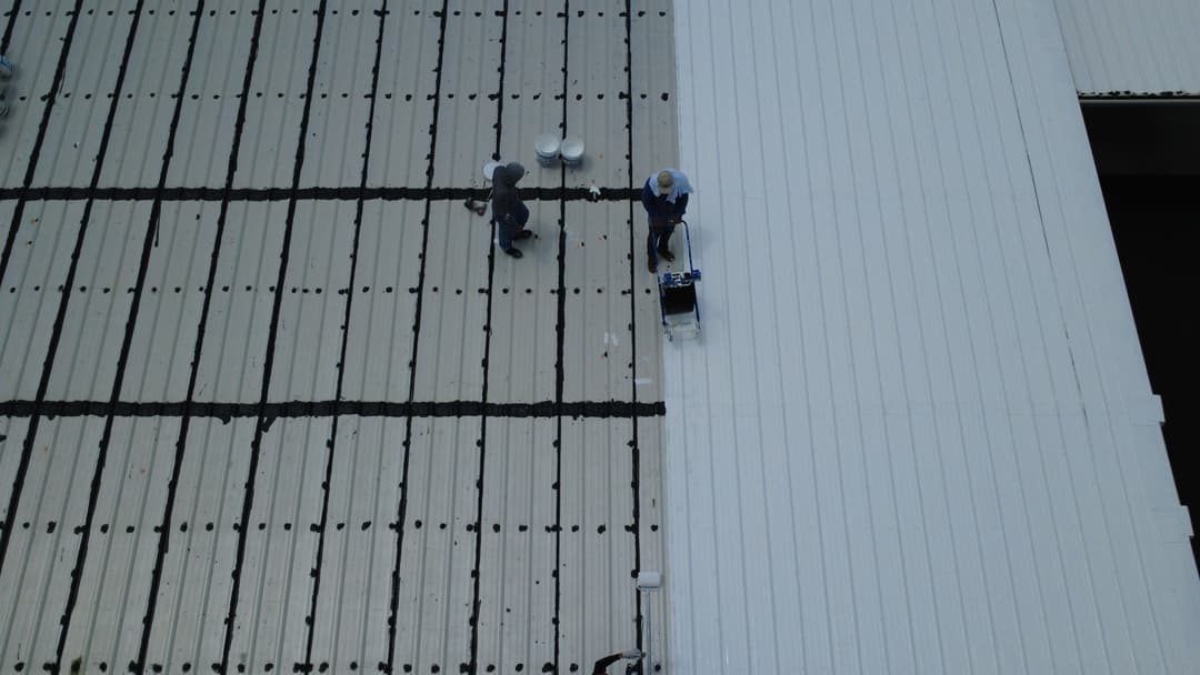 Workers performing maintenance on a commercial rooftop with metal panels.