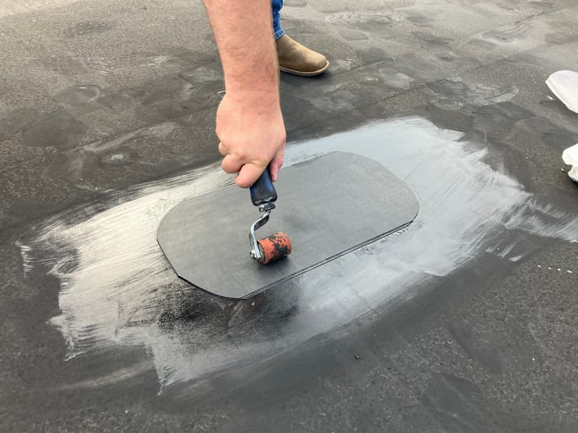 Person applying sealant with a paint roller on a flat rooftop surface.